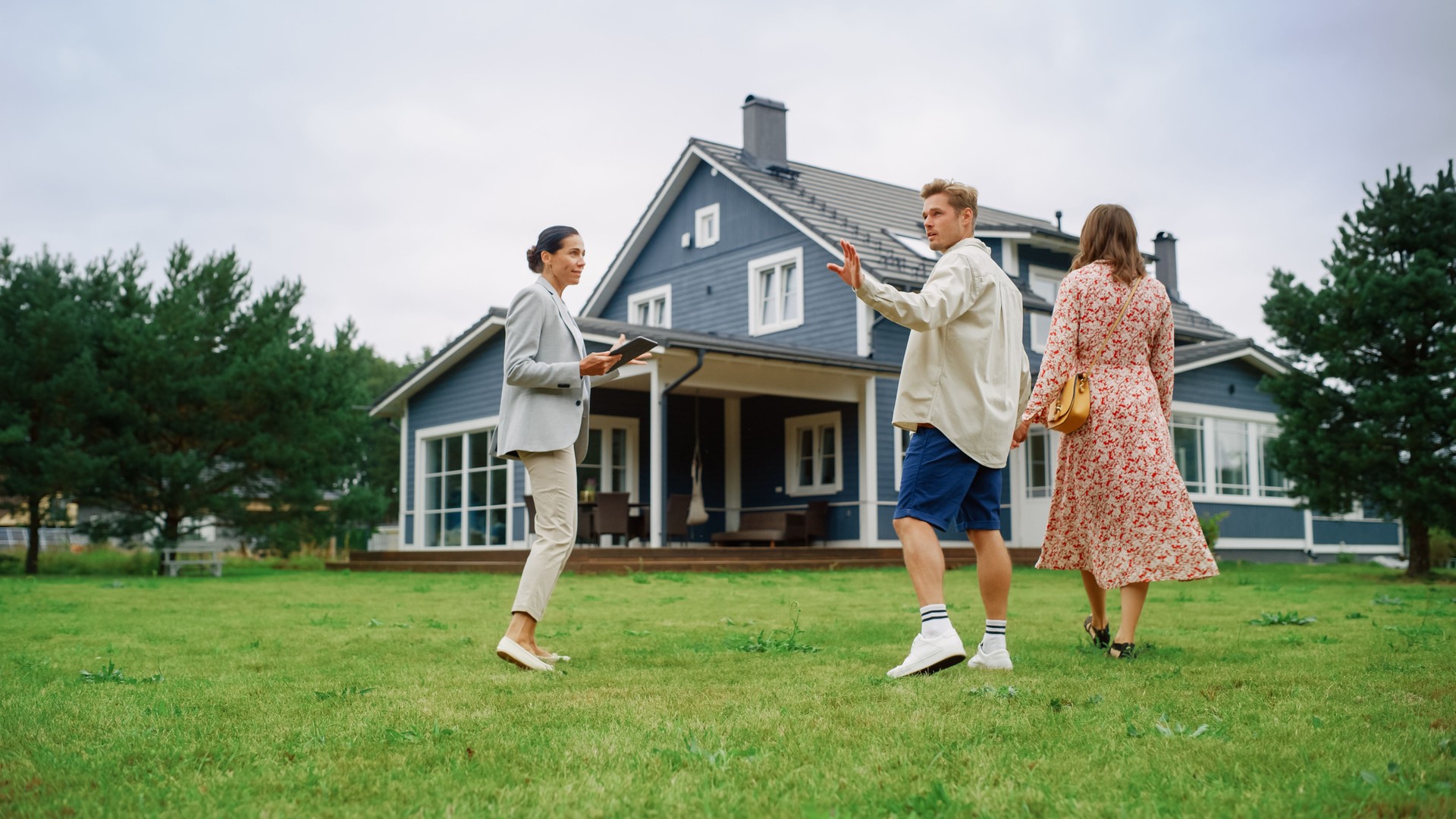 Young Couple Visiting a Potential New Home Property with Professional Real Estate Agent. Female Realtor Showing the House to Future Homeowners. Focus on For Sale Sign.